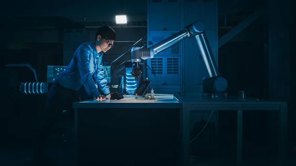 L'ingegnere giapponese sta testando un'interfaccia di intelligenza artificiale giocando a scacchi con un braccio robotico futuristico. Sono in un laboratorio di ricerca moderno ad alta tecnologia con luce a bassa chiave. — Foto Stock