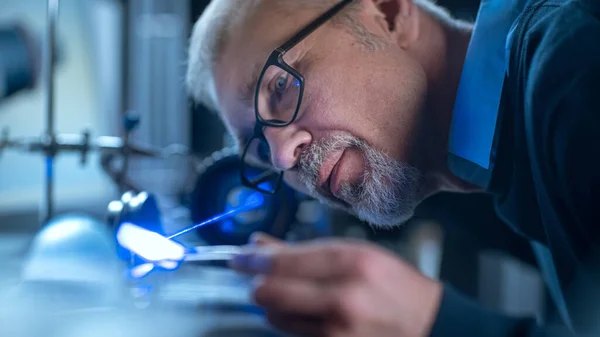 Portret z bliska Skupionego Inżyniera w Okularach pracującego z precyzyjnym urządzeniem laserowym, wykorzystującym soczewki i optykę testową dla dokładności Wymagana elektronika — Zdjęcie stockowe