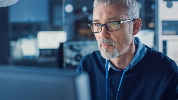 Ritratto di un bell'ingegnere di mezza età che indossa occhiali funziona su personal computer. Sullo sfondo High Tech Engineering Facility. — Foto Stock