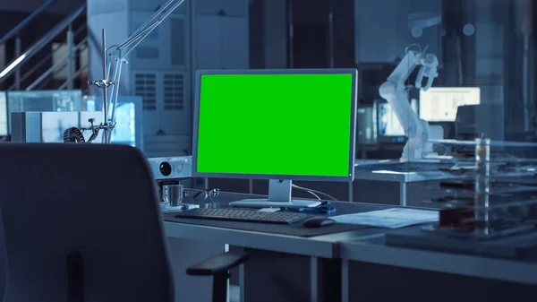 On the Desk Computer with Isolated Green Mock-up Screen Display. In the Background Robot Arm Concept Standing in Heavy the Dark.Industry Engineering Facility — Stock Photo, Image