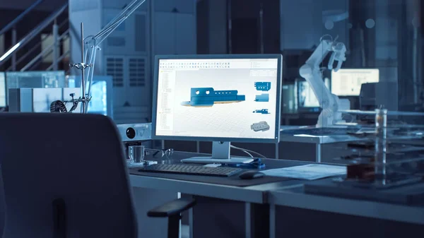 Op de bureaucomputer met CAD-software en ontwerp van 3D-componenten voor industriële machines. In de achtergrond Robot Arm Concept Standing in Heavy the Dark.Industry Engineering Facility. — Stockfoto