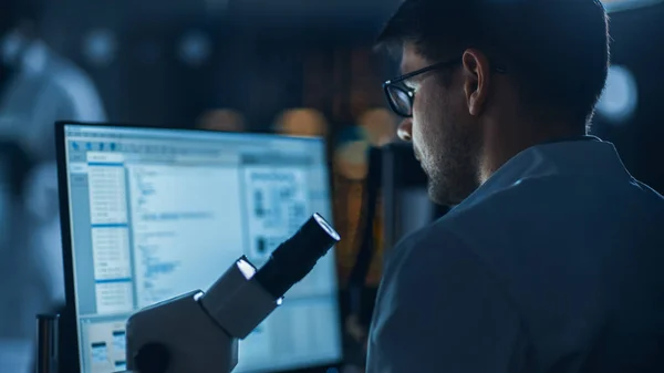 Shot of a Male IT Scientist Uses Computer Showing System Monitoring and Controlling Program (en inglés). En el Laboratorio de Desarrollo Tecnológico de Antecedentes con Científicos, Ingenieros trabajando — Foto de Stock