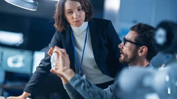 Ingénieur futuriste en développement de machines travaillant sur ordinateur à son bureau, parle avec une gestionnaire de projet féminine. Équipe de professionnels travaillant dans l'installation de design industriel moderne — Photo