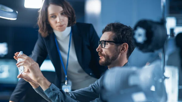 Ingénieur futuriste en développement de machines travaillant sur ordinateur à son bureau, parle avec une gestionnaire de projet féminine. Équipe de professionnels travaillant dans l'installation de design industriel moderne — Photo