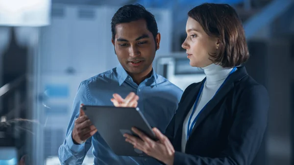 In Technology Research Facility: Nainen projektipäällikkö puhuu Chief Engineer, ne kuulla Tablet Computer. Team of Industrial Engineers, Kehittäjät työskentelevät moottorin suunnittelu Tietokoneiden avulla — kuvapankkivalokuva