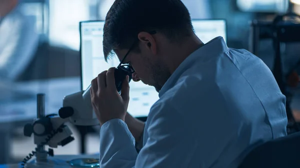 Shot of a Male IT Scientist Χρησιμοποιεί Υπολογιστή με Ηλεκτρονικό Μικροσκόπιο. Στο Εργαστήριο Ανάπτυξης Τεχνολογίας Φόντο με Επιστήμονες, Μηχανικούς που εργάζονται — Φωτογραφία Αρχείου