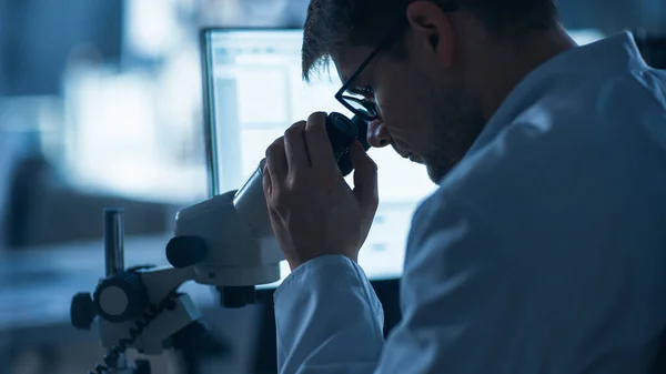 Shot of a Male IT Scientist Χρησιμοποιεί Υπολογιστή με Ηλεκτρονικό Μικροσκόπιο. Στο Εργαστήριο Ανάπτυξης Τεχνολογίας Φόντο με Επιστήμονες, Μηχανικούς που εργάζονται — Φωτογραφία Αρχείου