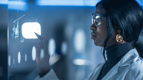스마트하고 아름다운 아프리카계 미국인 여성 과학자 Wearing White Coat and Protective Glasses Writes Formula on Glass Whiteboard, References Her Tablet Computer — 스톡 사진