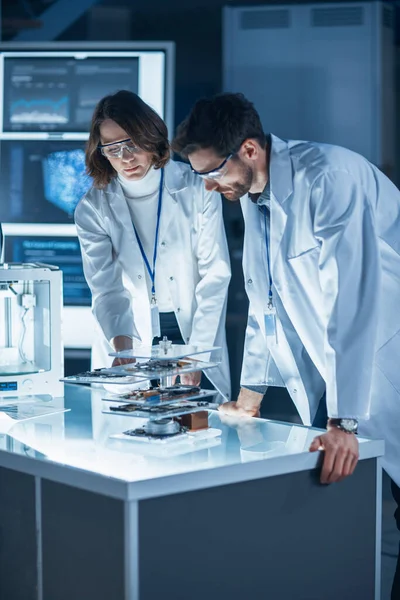 Diverse International Team of Industrial Scientists and Engineers Wearing White Coats Working on Heavy Machinery Design in Research Laboratory. Professionals Using 3D Printer, Computers and Microscope