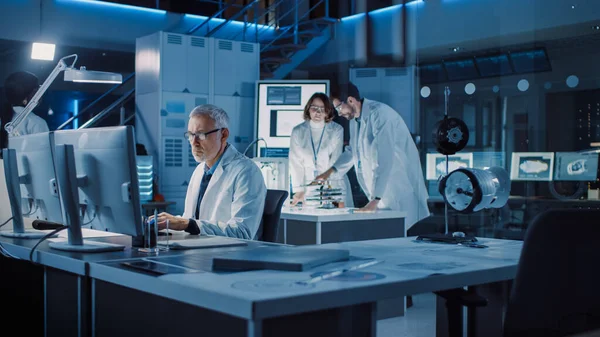 Diverse International Team of Industrial Scientists and Engineers Wearing White Coats Working on Heavy Machinery Design in Research Laboratory (em inglês). Profissionais usando computadores e conversando — Fotografia de Stock