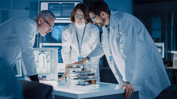 Снимок сделан в лаборатории промышленного дизайна, специалист использует микроскоп, конструктор работает на персональном компьютере, исследователь пишет на стеклянной доске, команда разработчиков использует 3D-принтер и материнскую плату