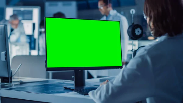 Över axeln skott: Kvinna IT-forskare använder grön Mock-up Screen Computer. I bakgrundsteknikens forsknings- och utvecklingslaboratorium med forskare, ingenjörer som arbetar med högteknologisk design — Stockfoto