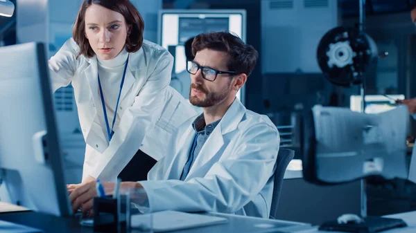 Makine Motor Geliştirme Mühendisi Masasında Bilgisayar üzerinde çalışıyor, Proje Yöneticisi ile konuşuyor, Prototip Bileşenini gösteriyor. Modern Endüstriyel Tasarım Laboratuvarı 'nda çalışan Profesyonel Ekip