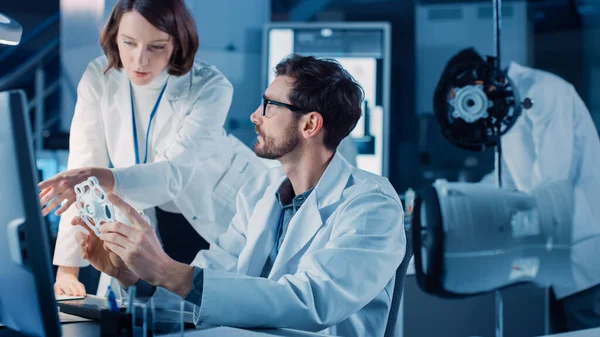 Ingénieur en développement de machines travaillant sur ordinateur à son bureau, discute avec le gestionnaire de projet, montre la composante prototype. Équipe de professionnels travaillant au Laboratoire de design industriel moderne — Photo