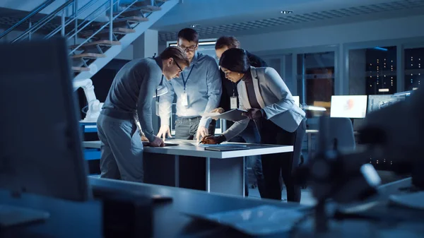 Diverse Team of Electronics Development Engineers Stojąc przy biurku pracując z dokumentami, rozwiązując problemy projektowe późno w nocy. Specjaliści pracujący nad Ultra Modern Industrial Design. — Zdjęcie stockowe