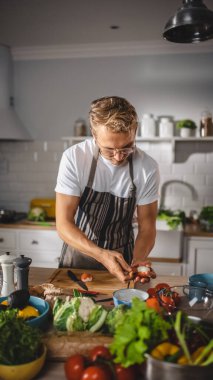 Beyaz Gömlekli ve Önlüklü Yakışıklı Modern Sunny Kitchen 'da Sağlıklı Organik Salata Yemekleri Yapıyor. Gözlüklü hippi aşçı. Doğal Temiz Diyet ve Sağlıklı Yaşam Konsepti.
