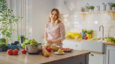 Çizgili Kazaklı Genç Kadın, Modern Sunny Kitchen 'da Sağlıklı Organik Salata Yapıyor. Otantik Kadın Karnabahar 'ı bıçakla doğruyor. Kameraya bakar ve gülümser..