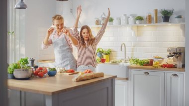 Pembe Gömlekli Yakışıklı Genç Adam ve Önlüklü Güzel Kız Mutfakta Yaratıcı Dans Ediyor. Sağlıklı Yeşil Sebzeli Sunny Modern Kitchen. Mutlu Çift Evde