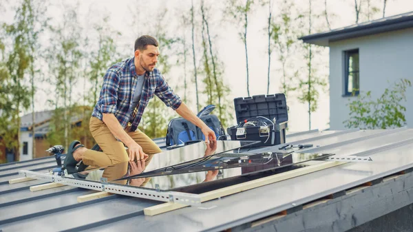 Caucasian Man in Checkered Shirt installeert Black Reflective Solar Panels op een metalen basis. Hij werkt op een dak op een zonnige dag. Het concept van ecologische hernieuwbare energie thuis. — Stockfoto