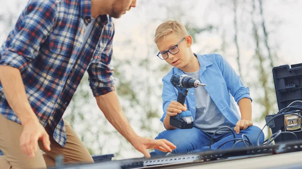 Far och son installerar solpaneler på en metallgrund. Son Passerar Borra till en Fader. De jobbar på ett tak på en solig dag. Begreppet ekologisk förnybar energi i hemmet och kvalitet familjetid. — Stockfoto