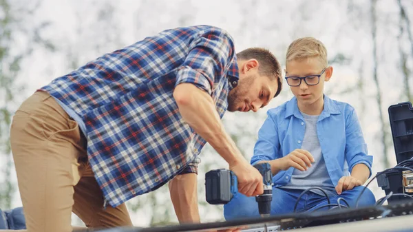 Padre e hijo instalando paneles solares en una base metálica con un taladro. Trabajan en un tejado de casa en un día soleado. Concepto de Energía Renovable Ecológica en el Hogar y Tiempo Familiar de Calidad. —  Fotos de Stock