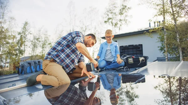 Padre e figlio Installazione di pannelli solari su una base metallica con un trapano. Lavorano su un tetto della casa in un giorno soleggiato. Concetto di energia rinnovabile ecologica a casa e qualità Family Time. — Foto Stock