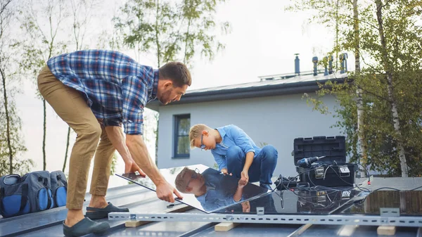 Padre e Hijo Instalando Paneles Solares a una Base Metal. Están sosteniendo los paneles en un tejado de la casa en un día soleado. Concepto de Energía Renovable Ecológica en el Hogar y Tiempo Familiar de Calidad. — Foto de Stock