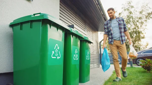 Vit man går utanför sitt hus för att ta ut två plastpåsar med skräp. En soppåse är sorterad med biologiskt matavfall, Andra är med återvinningsbara flaskor. Rädda miljön. — Stockfoto