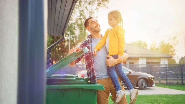 Iloinen isä piteli nuorta tyttöä ja heitti ruokajätteen roskiin. He käyttävät oikeita roskakoreja, koska tämä perhe lajittelee jätteitä ja auttaa ympäristöä. — kuvapankkivalokuva
