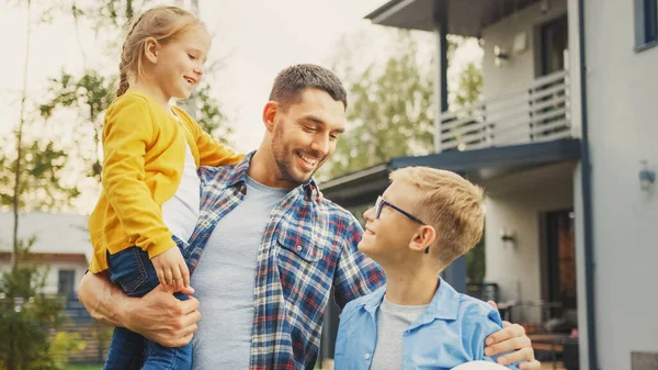 Onnellisen kolmen perheen muotokuva: Isä, tytär, poika. He poseeraavat kameran edessä nurmikolla lähellä Country House. Isä pitelee tyttöä sylissään. Poika pitelee jalkapalloa. — kuvapankkivalokuva