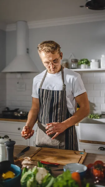 Pohledný muž v bílé košili a zástěře je dělat zdravé bio salát jídlo v moderní slunné kuchyně. Hipster Man in Glasses Cooking. Natural Clean Diet and Healthy Way of Life Concept. — Stock fotografie