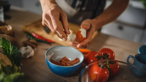 Schöner Mann schält grüne Frühlingszwiebeln mit den Händen. Der Mann in weißem Hemd und Schürze bereitet in einer modernen, sonnigen Küche eine Bio-Salatmahlzeit zu. Natürliche saubere Ernährung und gesunder Lebensstil. — Stockfoto