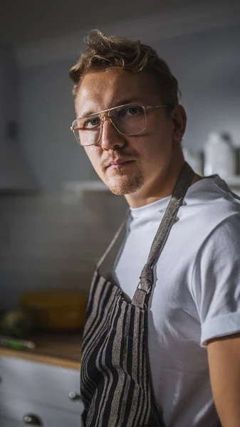 一个穿着白衬衫的英俊厨师的肖像镜头和一个明亮的现代厨房里放相机的阿普龙镜头。戴眼镜的嬉皮士人自然清洁饮食、健康生活方式概念 — 图库照片