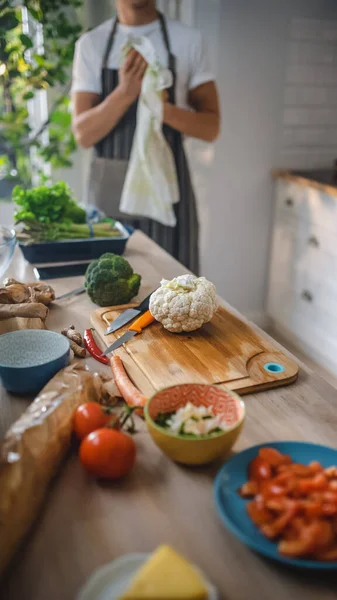 まな板の上に野菜やカリフラワーとキッチンテーブルのショット.現代の日当たりの良いキッチンで健康的なオーガニックグリーンフード。自然食と健康的なライフスタイルのコンセプト. — ストック写真