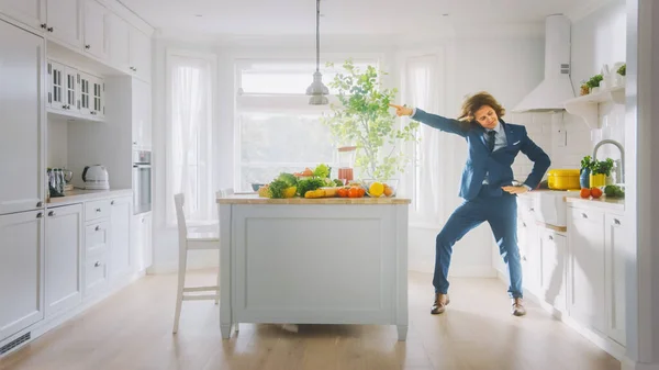 Mutfakta Uzun Saçlı, Enerjik Komik Genç Adam Mavi Takım Elbiseyle Dans Ediyor. Masadaki Sağlıklı Yeşil Sebzelerle Parlak Beyaz Modern Mutfak Bölgesi. Samimi Ev. — Stok fotoğraf