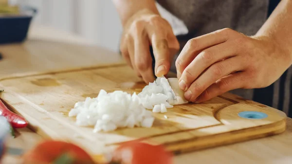 Nahaufnahme eines Mannes, der mit einem scharfen Küchenmesser eine Zwiebel zerhackt. Die Zubereitung einer gesunden biologischen Mahlzeit in einer modernen Küche. Natürliche saubere Ernährung und gesunder Lebensstil. — Stockfoto