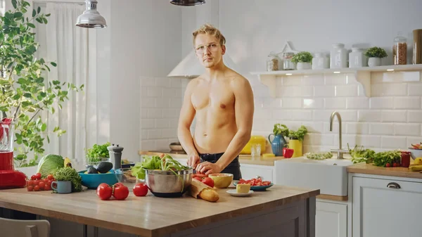 Homem sem camisa bonito cortando uma cenoura com uma faca de cozinha afiada. Preparando uma refeição saudável de salada orgânica em uma cozinha moderna. Topless Masculino na Dieta. — Fotografia de Stock
