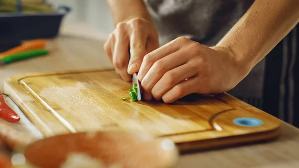 Nahaufnahme eines Mannes, der eine grüne Chilischote mit einem scharfen Küchenmesser hackt. Zubereitung einer gesunden Bio-Salatmahlzeit in einer modernen Küche. Natürliche saubere Ernährung und gesunder Lebensstil. — Stockfoto