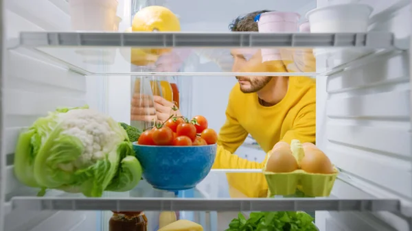 Drinnen im Kühlschrank: Junger bärtiger Mann zückt Wasserflasche Gesunder Mann bleibt hydratisiert. POV-Aufnahme aus dem Kühlschrank voller gesunder Lebensmittel, Lebensmittel, Joghurt — Stockfoto