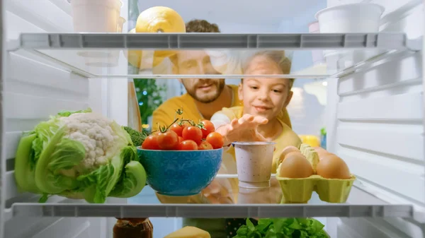 Câmera dentro da cozinha Frigorífico: Pai levanta pequena filha bonito para escolher o que quer que ela quer tirar da geladeira, Ela escolhe iogurte saudável. Ponto de vista POV tiro da geladeira cheia de alimentos — Fotografia de Stock