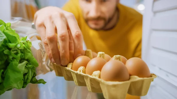 Shot from Inside Kitchen Fridge: Fešák otevře ledničku, podívá se dovnitř Vezme pár vajec z krabice s vejci. Muž připravující zdravé jídlo. Pohled POV Shot z chladničky plné zdravých potravin — Stock fotografie