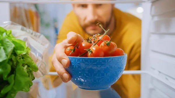 Caméra à l'intérieur de la cuisine Frigo : bel homme ouvre la porte du réfrigérateur, sort bol de tomates. Homme préparant un repas sain. Point de vue POV Tourné depuis un réfrigérateur rempli d'aliments sains — Photo