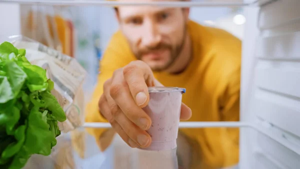 Câmera dentro da cozinha Frigorífico: Homem bonito abre a porta do frigorífico, tira iogurte. Homem a comer saudável. Ponto de vista POV tiro da geladeira cheia de alimentos saudáveis — Fotografia de Stock