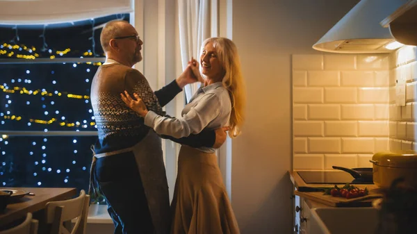 Senior Couple i Love Have Romantic Evening, Dancing in the Kitchen, Celebrating Anniversary (engelsk). Eldre har romantisk kveld med vin, festlig bord i kjøkken og kjøkken.. – stockfoto