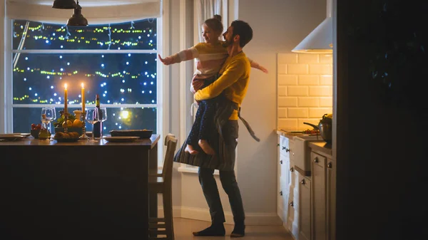 Gelukkige vader en dochter die samen koken en dineren. Vader bereidt eten, knuffelt schattig klein meisje. Feestelijke tafel in stijlvol keukeninterieur met warm licht — Stockfoto