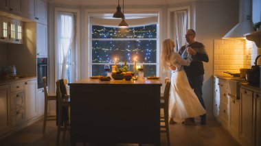 Mutlu Son Sınıf Çifti Romantik Bir Gece Geçiriyor, Mutfakta Dans Ediyor, Yıldönümünü Kutluyor. Yaşlı, sevimli koca, eş Şık Mutfak İçlerinde Şenlikli Masayla Romantik Bir Akşam Geçirin
