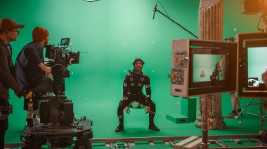 In the Big Film Studio Professional Crew Shooting Blockbuster Movie. Director Commands Camera Operator to Start shooting Green Screen CGI Scene with Actor Wearing Motion Tracking Suit and Head Rig clipart