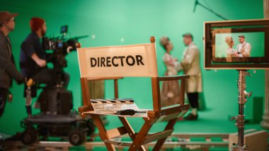 On Film Studio Set Focus on Empty Directors Chair. In the Background Professional Crew Shooting Historic Movie, Cameraman on Railway Trolley Shooting Green Screen Scene with Actors for History Movie clipart