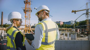Erkek İnşaat Mühendisi ve Genç Kadın İnşaat Mimarı Şehir İnşaat Alanında Tablet Bilgisayar Kullan. Gayrimenkul Geliştirme ve Planlamanın Geleceği hakkında konuşuyorlar. Güvenlik Şapkası Giymek.
