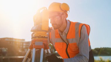 İnşaat İşçisi İnşaat Alanındaki Yatay ve Dikey Düzlemlerdeki Açıları Ölçmek İçin Optik Araştırma Aracı Kullanıyor. Bina için Sert Şapka Yapımında İşçi Projeksiyonu.